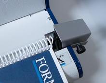 Load image into Gallery viewer, Close-up of a spiral-bound notebook being fed through a binding or scoring machine. The notebook cover is dark blue with white text reading 'FORM', and the machine has a white and blue body with a gray roller assembly.