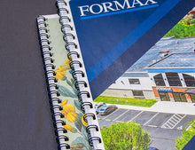 Load image into Gallery viewer, A close-up of a spiral-bound booklet or manual showing printed company branding. The visible text reads FORMAX, with a blue cover and part of another printed page showing a building exterior and parking lot.