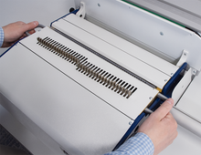 Load image into Gallery viewer, Close-up of a person's hands adjusting a white and blue binding machine with a slotted guide rail, set against a clean white industrial background.