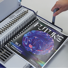 Load image into Gallery viewer, A hand inserts a magazine or book titled "FUTURES" into a white spiral binding machine. The cover features a glossy, abstract blue and purple brain-like graphic on a dark background.